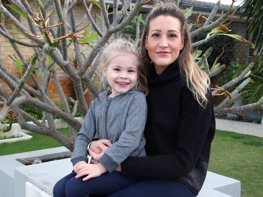 Brie sits with her daughter in front of a frangipani tree.