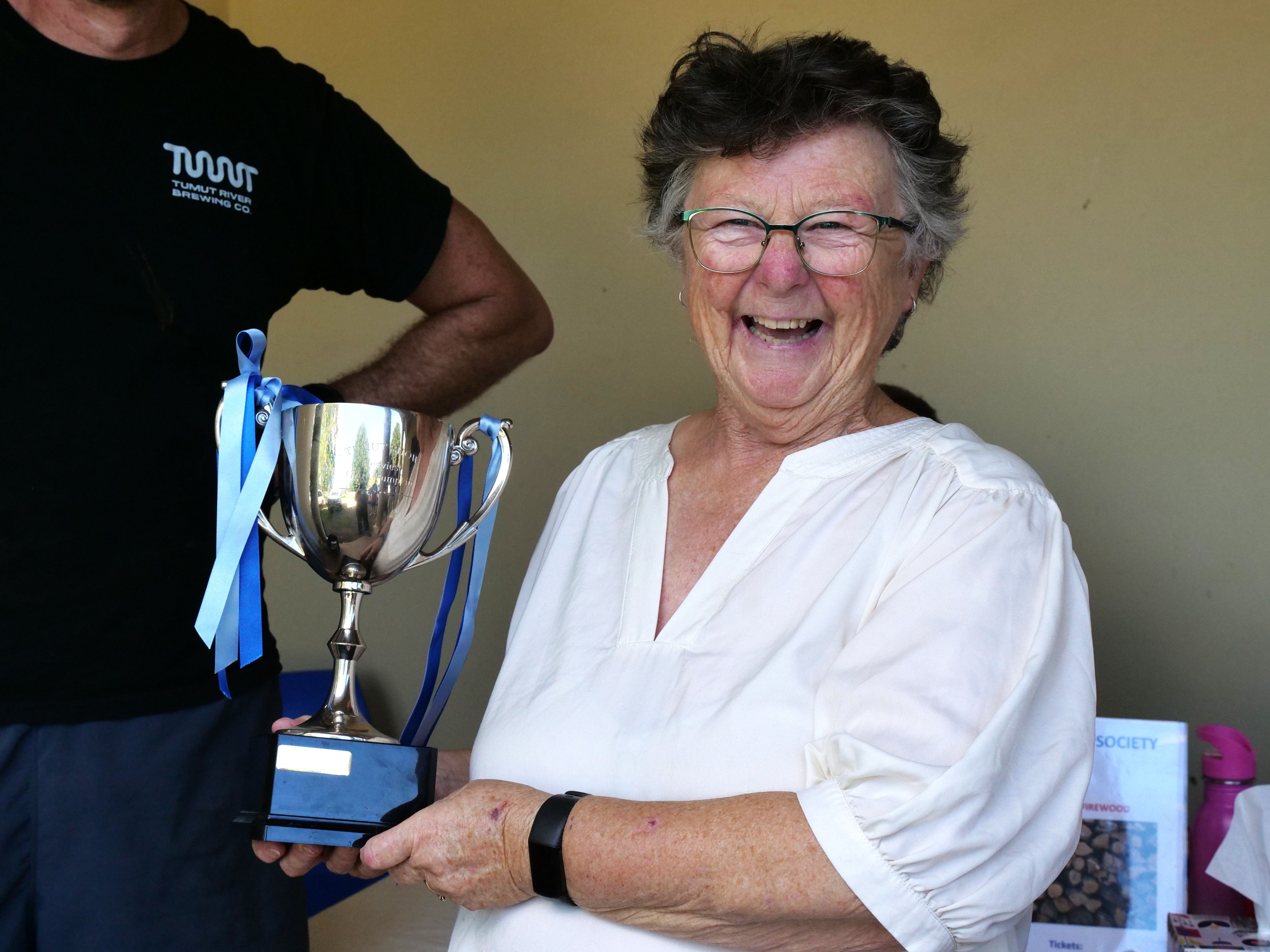 Mujer con camisa blanca sonriendo y sosteniendo un trofeo en forma de taza