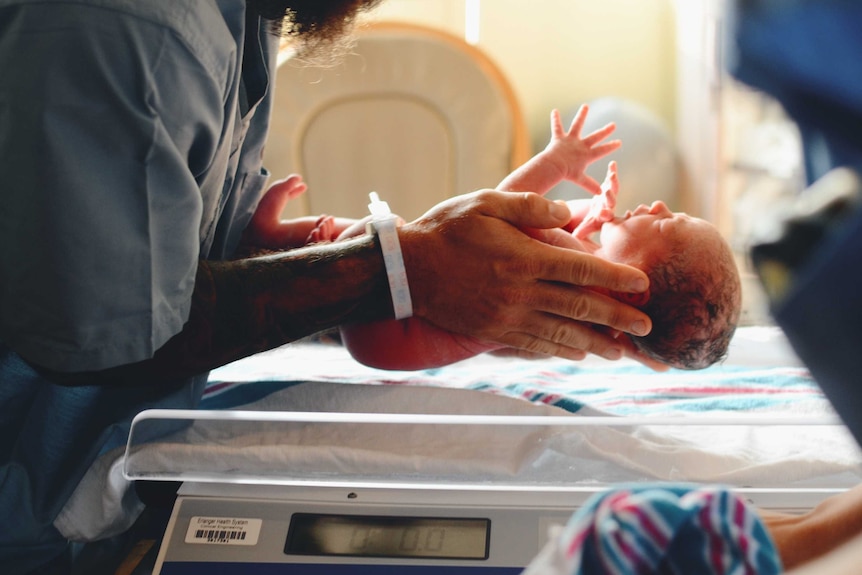 A man is gently holding a newborn baby and lying the baby on a blanket