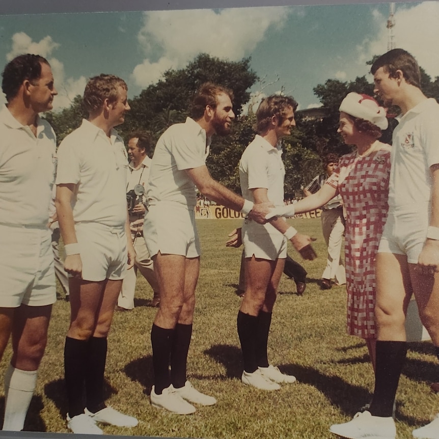 line of umpires wearing white with black long socks meeting the queen on a sporting field