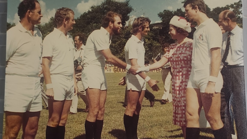 line of umpires wearing white with black long socks meeting the queen on a sporting field