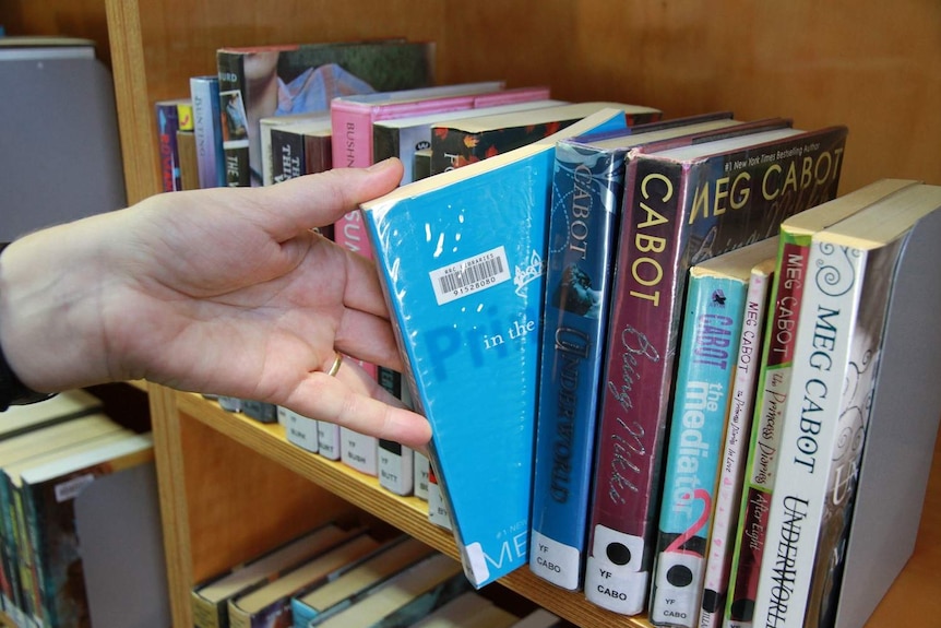 Books by author Meg Cabot on a library shelf.