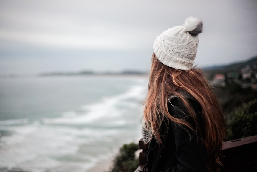 Girl in beanie looks out across storm skies