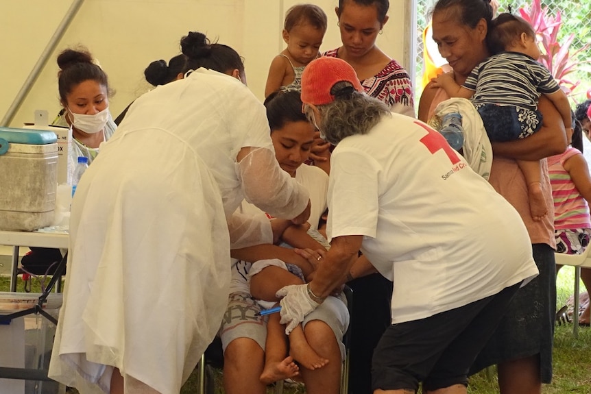 A woman gets her child vaccinated for measles at the Red Cross compound in Apia