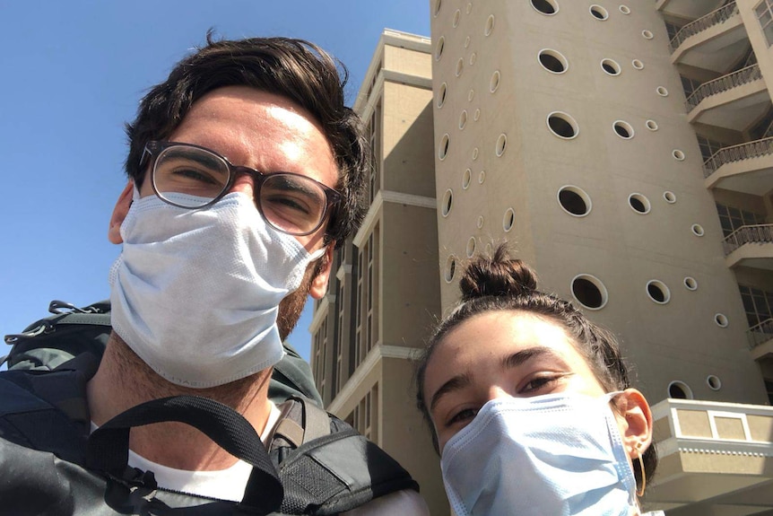 A young couple taking a selfie in face masks outside an apartment building