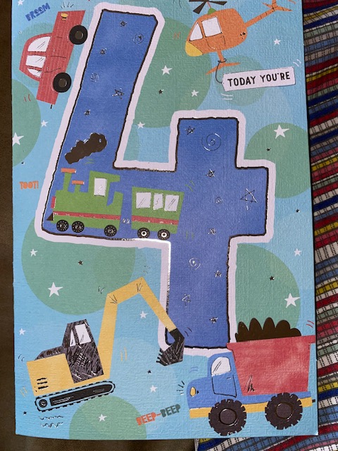 A blue birthday card for a four year old with colourful trucks on it