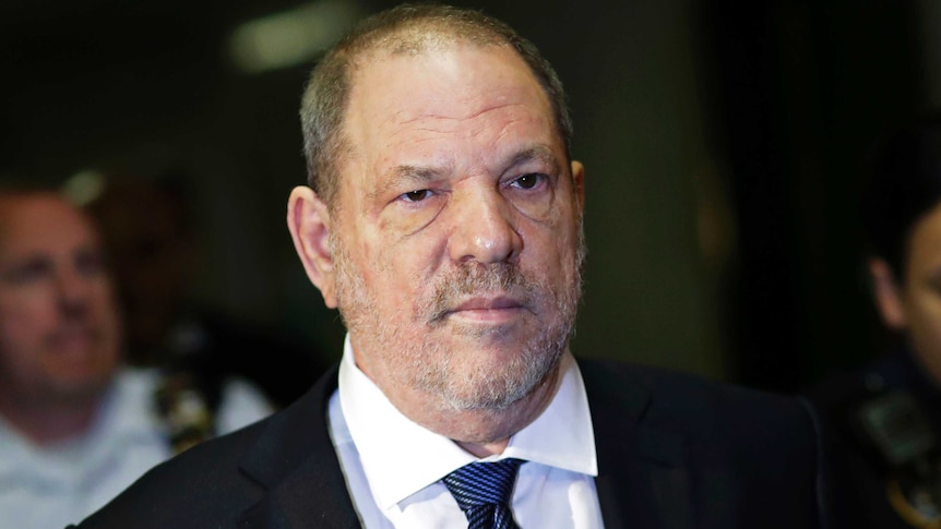Harvey Weinstein wears a black suit, white shirt and blue tie and looks to the right