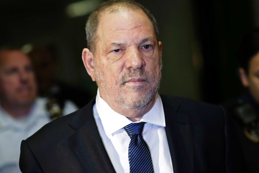 Harvey Weinstein wears a black suit, white shirt and blue tie and looks to the right