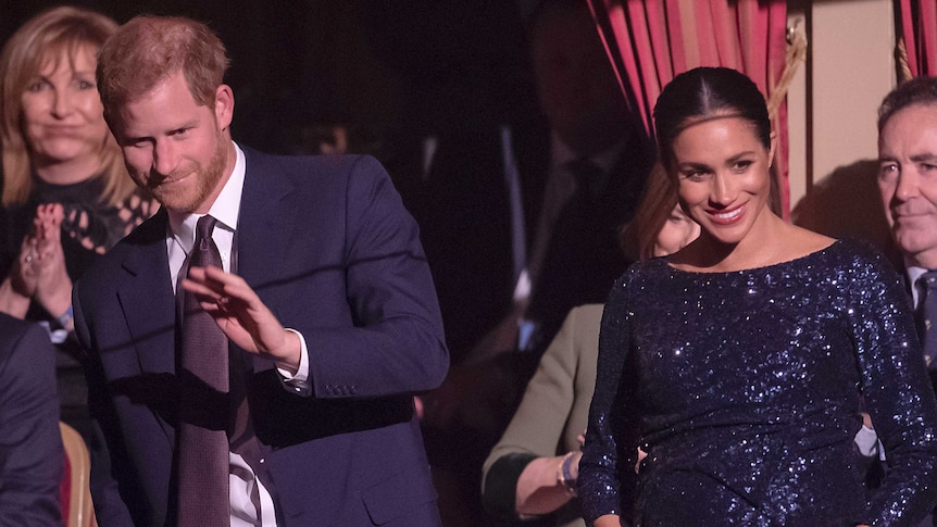 A couple in formal wear clap and smile in box seats