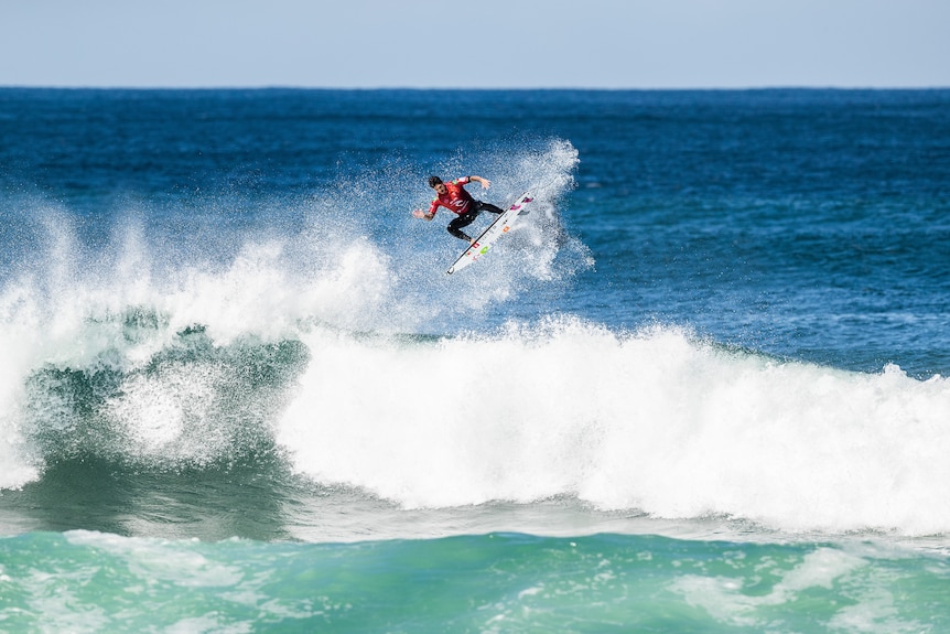 A male surfer rides his board in the air above a wave.