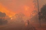 A firefighter walks along a street with a blood red sky and smoke behind him.