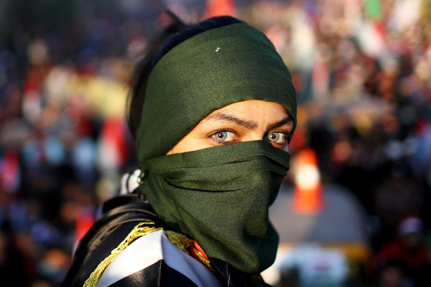 A woman protester with striking green eyes and a green hijab stars into the camera lens.