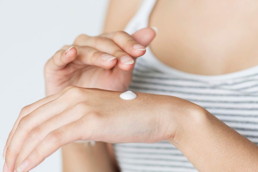 A woman applies cream to her hand.