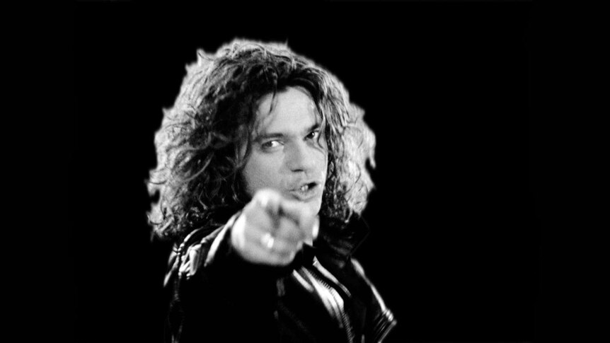 Black and white photo of Michael Hutchence looking straight into the camera pointing his finger.