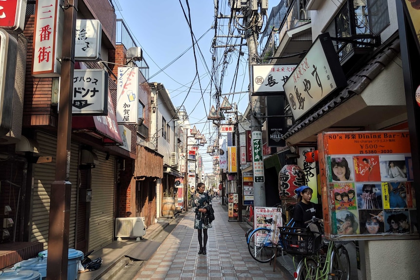 A woman stands in the middle of a colourful Japanese street underneath a tangle of wires.