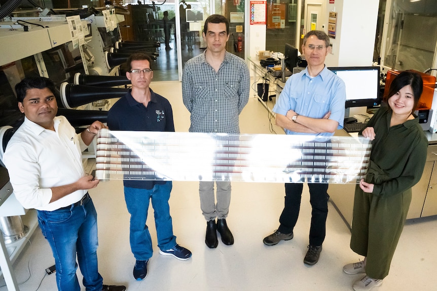 Cinq membres d'une équipe dans un laboratoire tenant un rouleau déroulé de biocapteurs imprimés