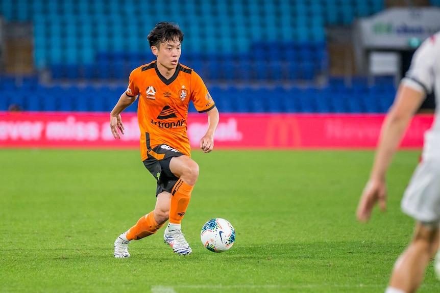 Danny Kim runs with the ball at his feet wearing an orange football kit