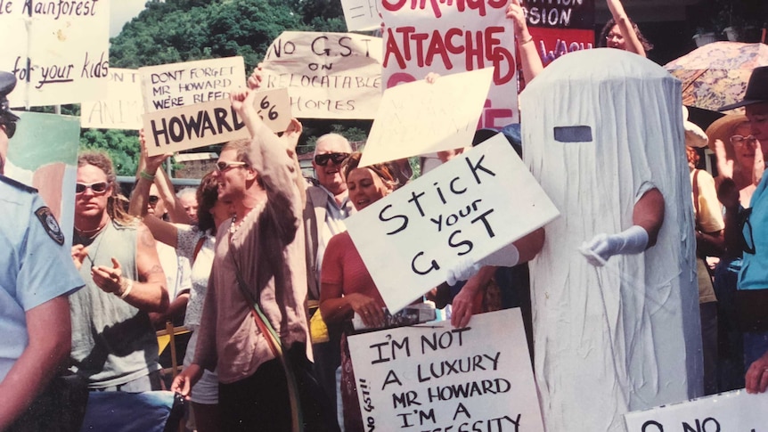 Rhonda Ellis dressed as Tania Tampon holds a sign saying "Stick your GST" at a protest confronting John Howard in 2000.