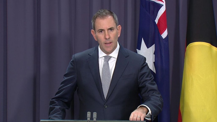 The Treasurer stands in front of an Australian and an Aboriginal flag at a press conference