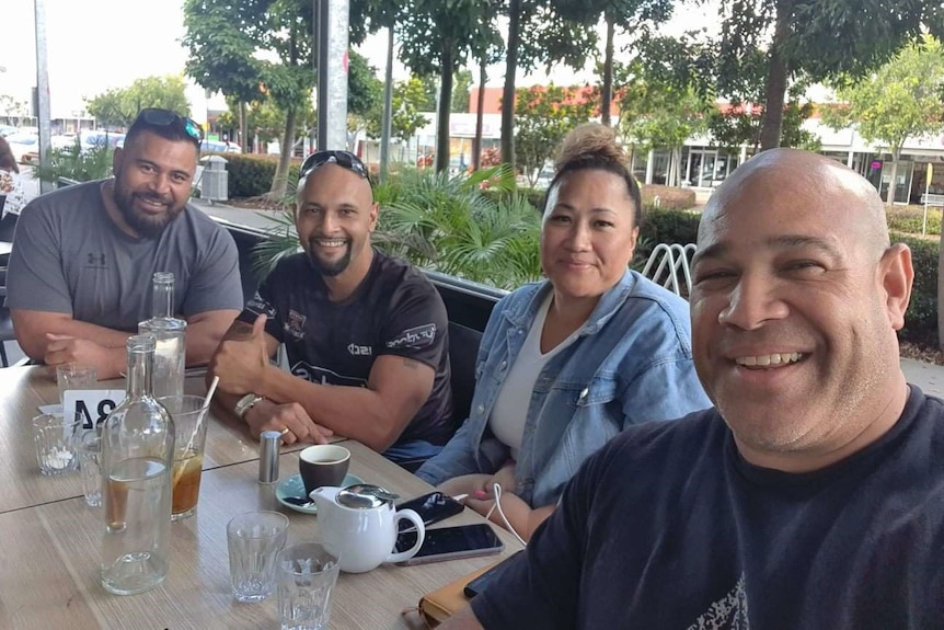 A man sits a cafe smiling with several other people