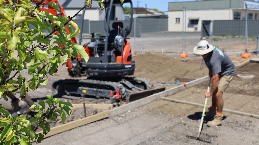 A builder shovels gravel next to a digger.