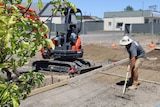 A builder shovels gravel next to a digger.
