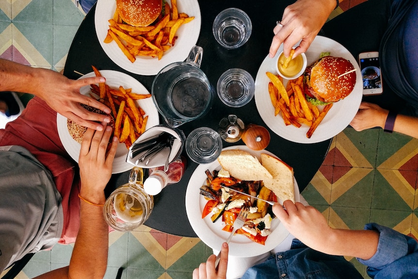 Generic image of four people sitting around a cafe table eating burgers and fries.