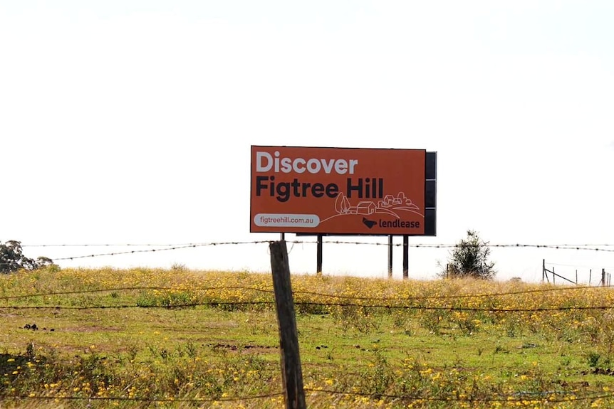 A sign in a field, behind a barbed wire fence, that reads "Discover Figtree Hill".