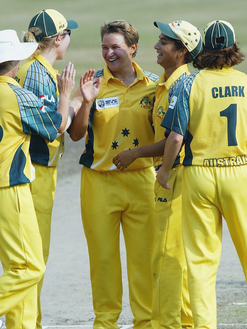A smiling Australian bowler is surrounded by her teammates after taking a wicket.