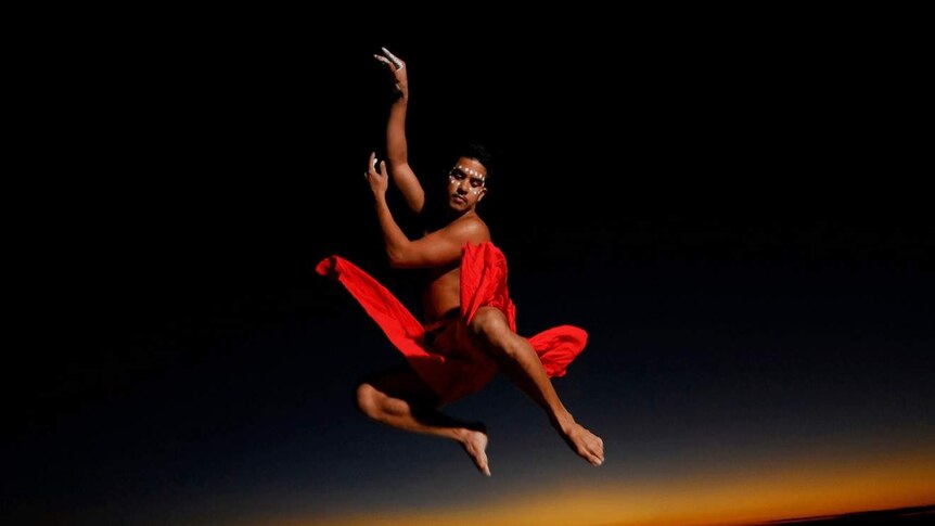 A man wearing a red cloth around his waist soars high in the air against a black background