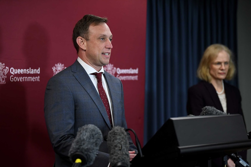 Steven Miles stands at a lectern in front of microphones.