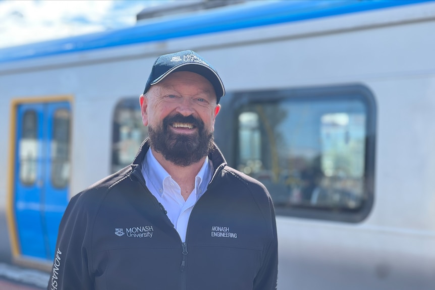 A bearded man smiling in front of a train