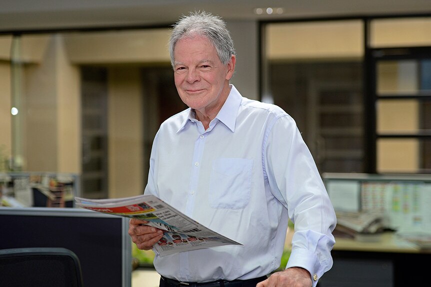 A man smiles while holding a newspaper.