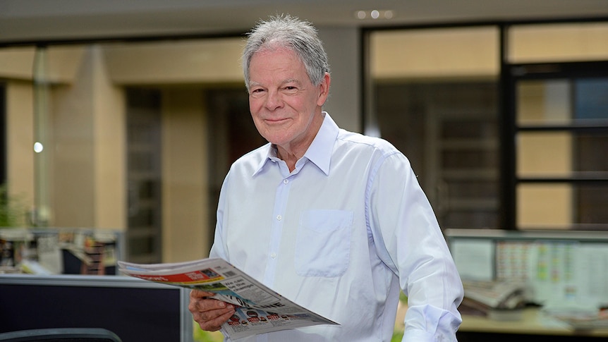 A man smiles while holding a newspaper.