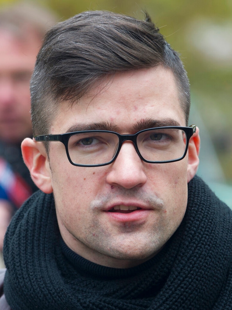 A man with a dark hair wearing a black scarf and black-rimmed glasses