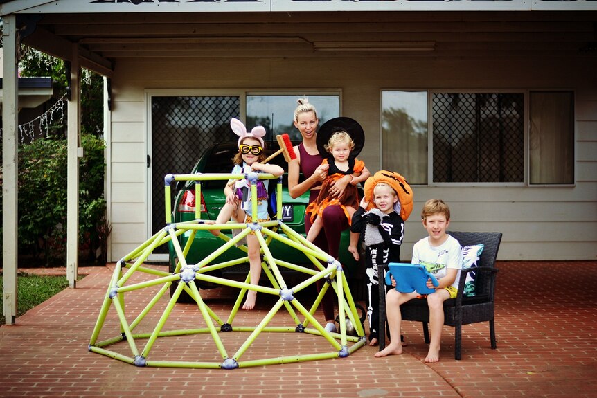 Four children in dress ups stand near play equipment with adult carer.