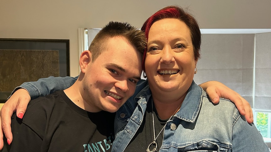 A woman with short red hair poses with her arm around her teenage son