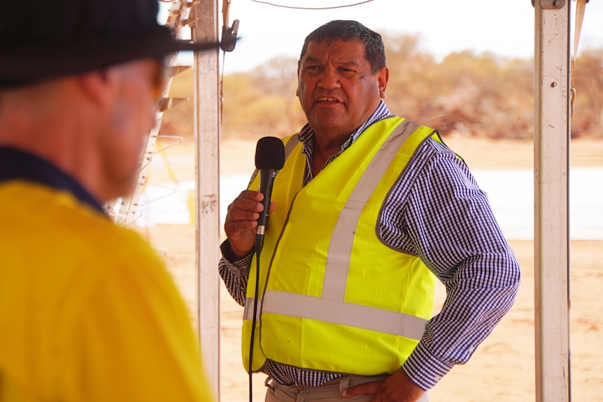 Des Mongoo in a high-vis vest, speaking into a microphone.