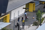 Travellers wearing masks wheel their suitcases along the front of a terminal building at Melbourne Airport.