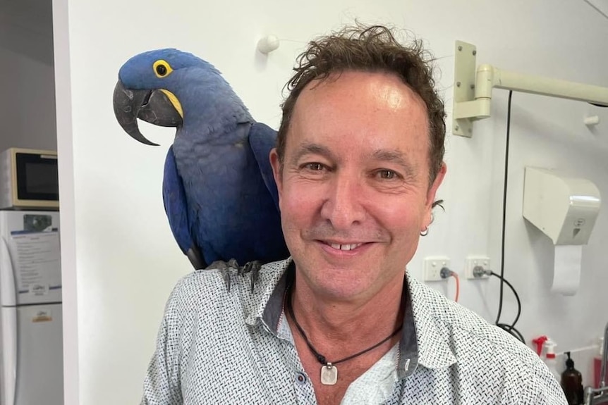 Man smiling with large blue bird on his shoulder. 