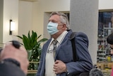 A man wearing a face mask walks away, ignoring cameras.