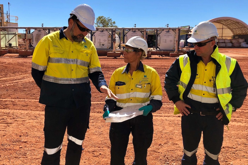 Three mine staff wearing yellow high vis clothing and hard hats at mine
