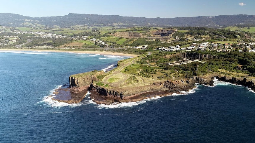 An aerial view of Bombo Headland, jutting out with a flat rock shelf below it and green countryside in the background.