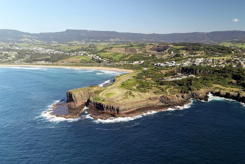 An aerial view of Bombo Headland, jutting out with a flat rock shelf below it and green countryside in the background.