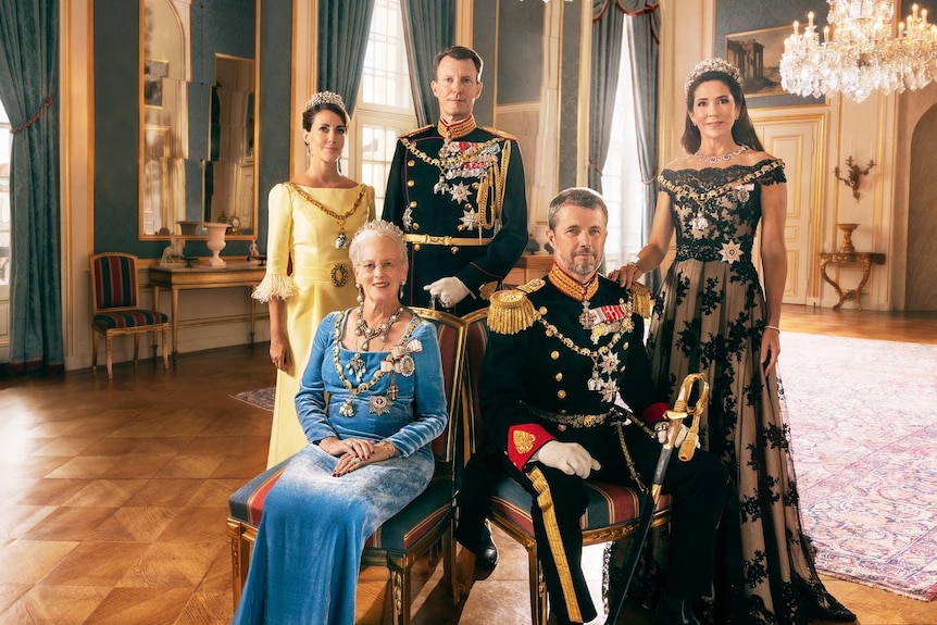 Five people in royal attire pose for a portrait, Queen Margrethe and Prince Frederik are seated at front adorned in jewels