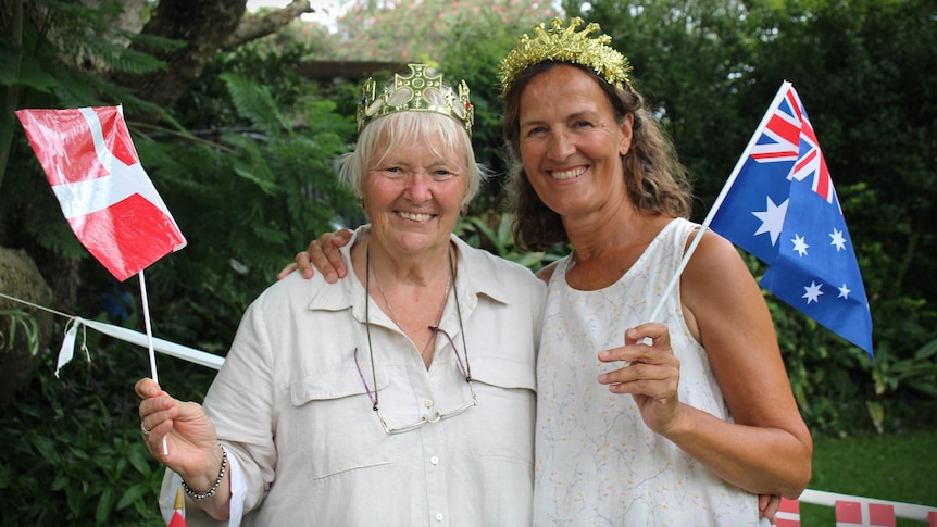 Two women wearing fake crowns wave miniature Australian and Danish flags.