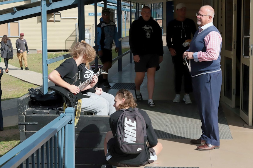 A teacher stands next to pupils on school grounds