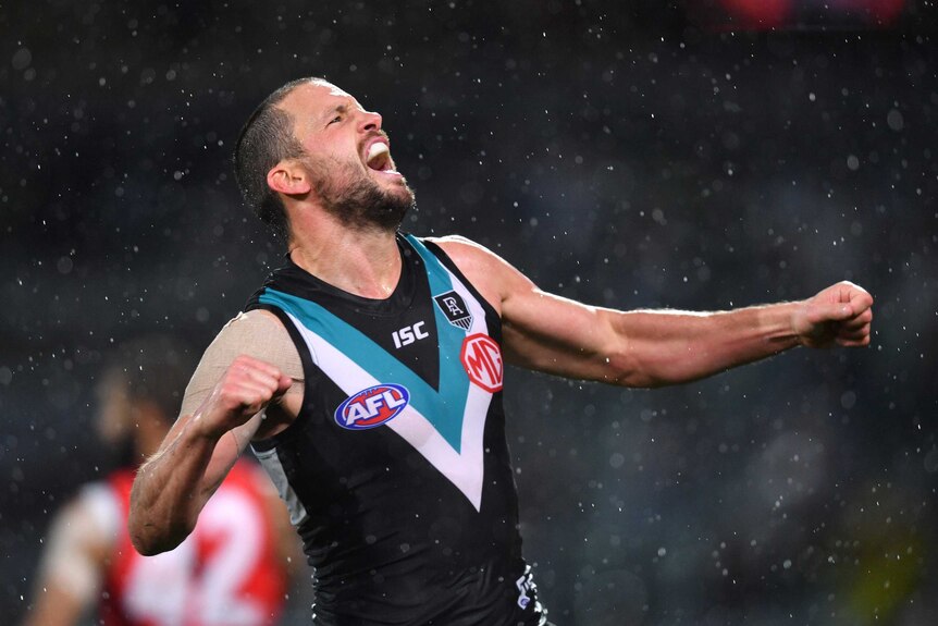 A Port Adelaide AFL player pumps his right fist in the rain after kicking a goal against the Bombers.