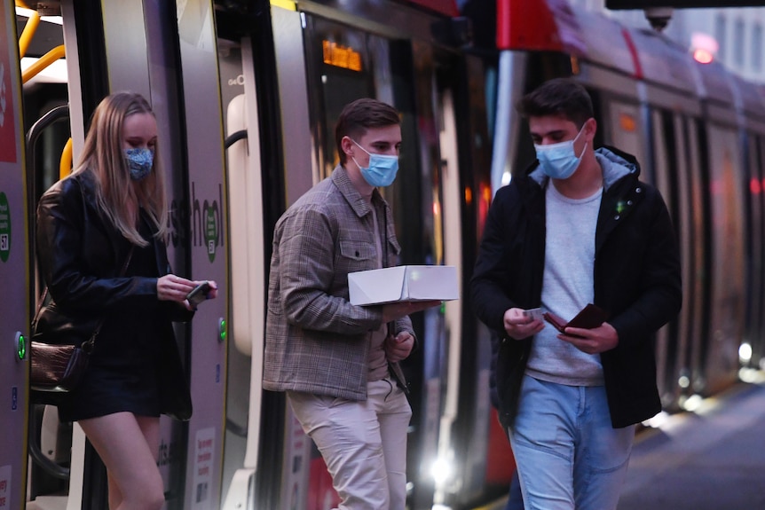 people wearing masks getting off a light rail