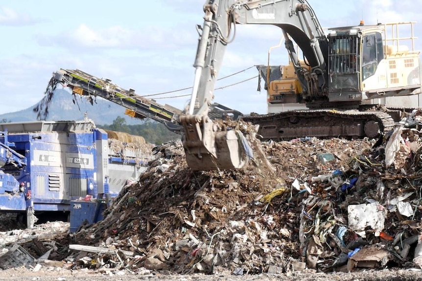 A tractor sits on top of a mountain of brown rubbish.